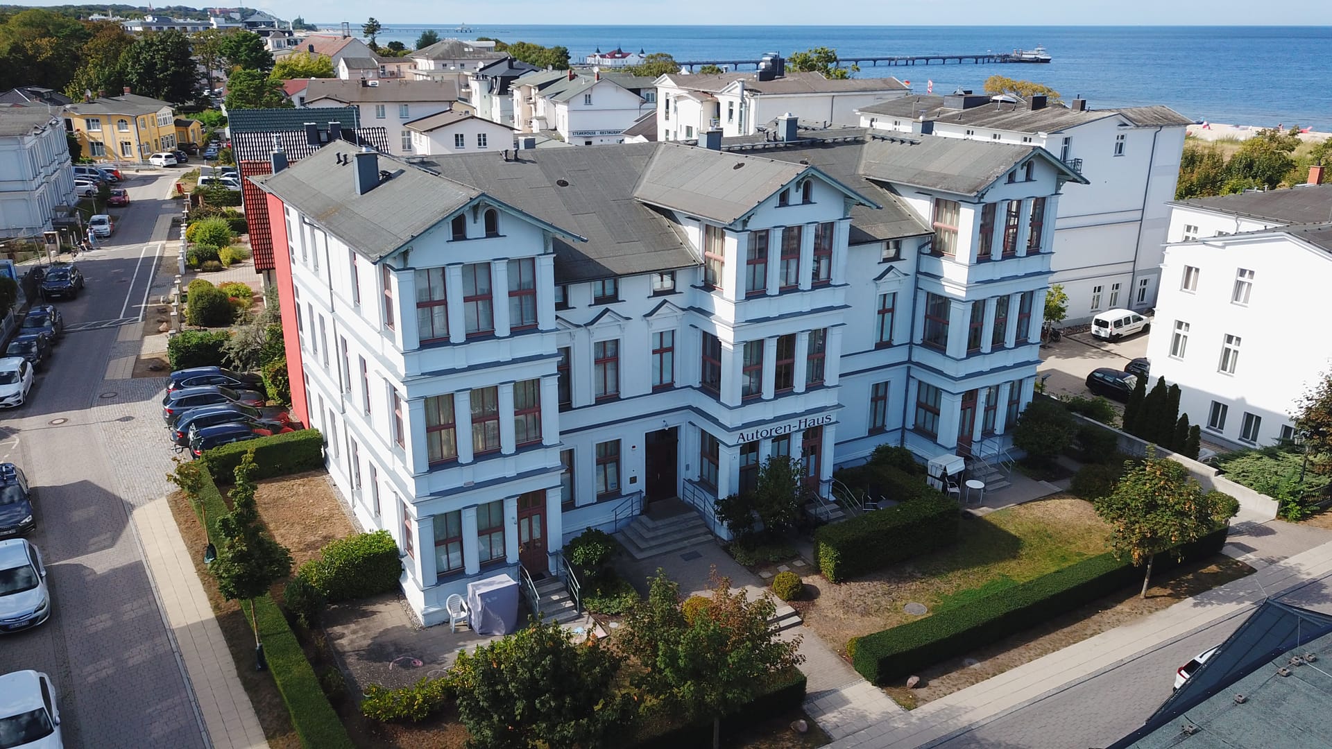 Luftaufnahme des Autorenhauses Ahlbeck – weiße Bädervilla mit Ostsee und Seebrücke im Hintergrund