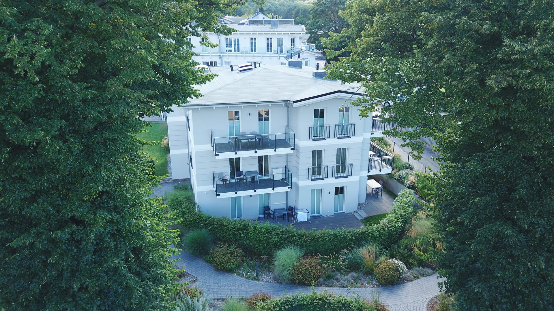 Gartenansicht des Domizil Meerzeit Ahlbeck zwischen alten Bäumen mit geschwungenen Wegen