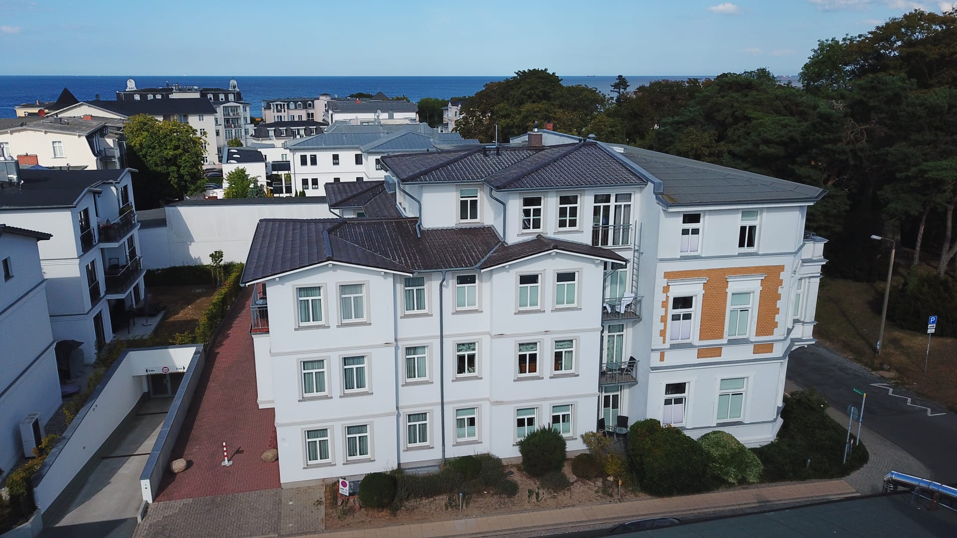 Luftaufnahme vom Haus am Kurpark Ahlbeck – weiße Bädervilla mit gelben Klinkerakzenten, dahinter die Ostsee