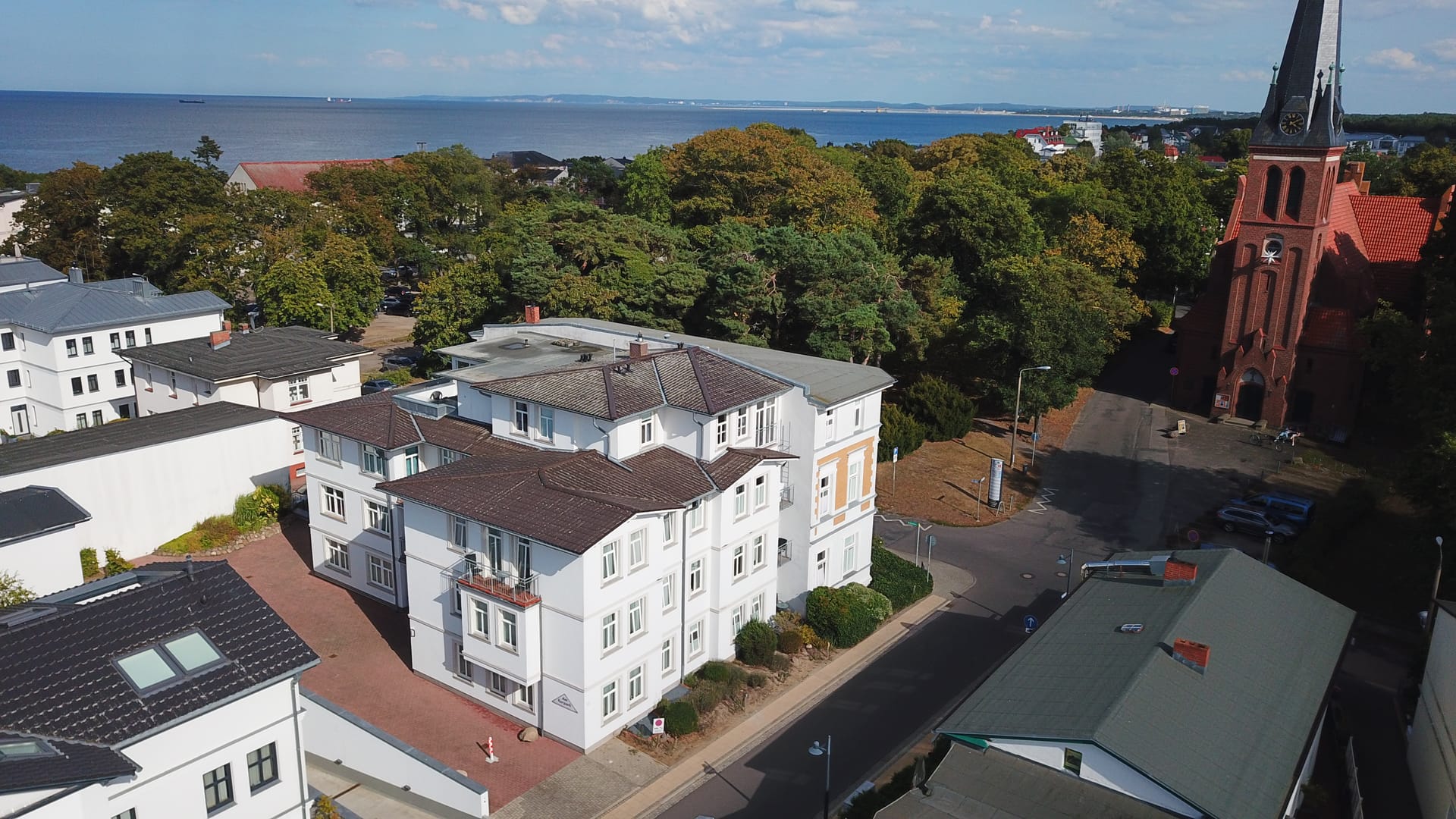 Panorama über die Dächer von Ahlbeck: Haus am Kurpark neben der Kirche, am Horizont die Ostsee