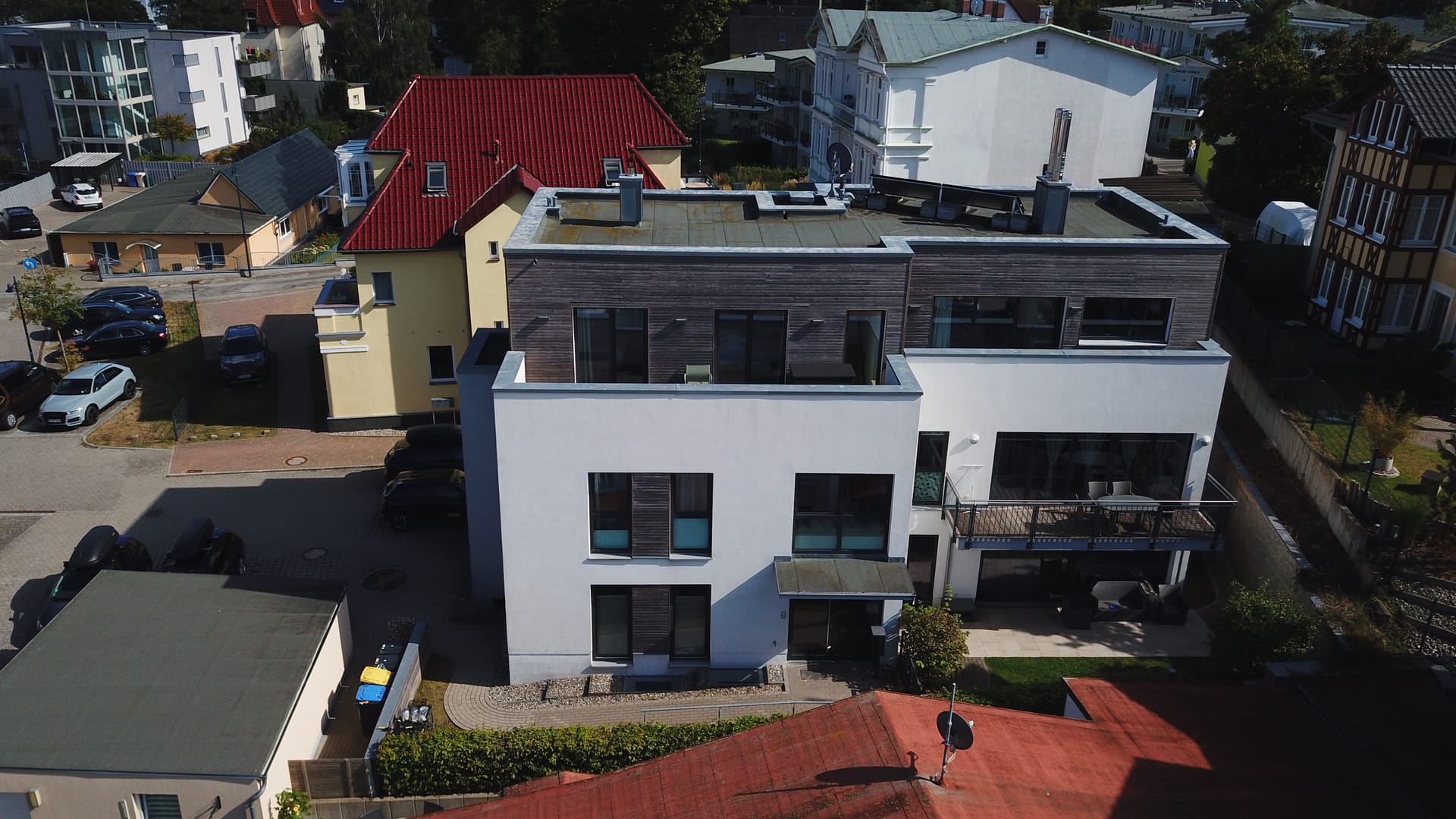 Quartier Ahlbeck von der Straßenseite – weiße Fassade mit grauen Holzakzenten, Balkonen und Stellplätzen am Haus