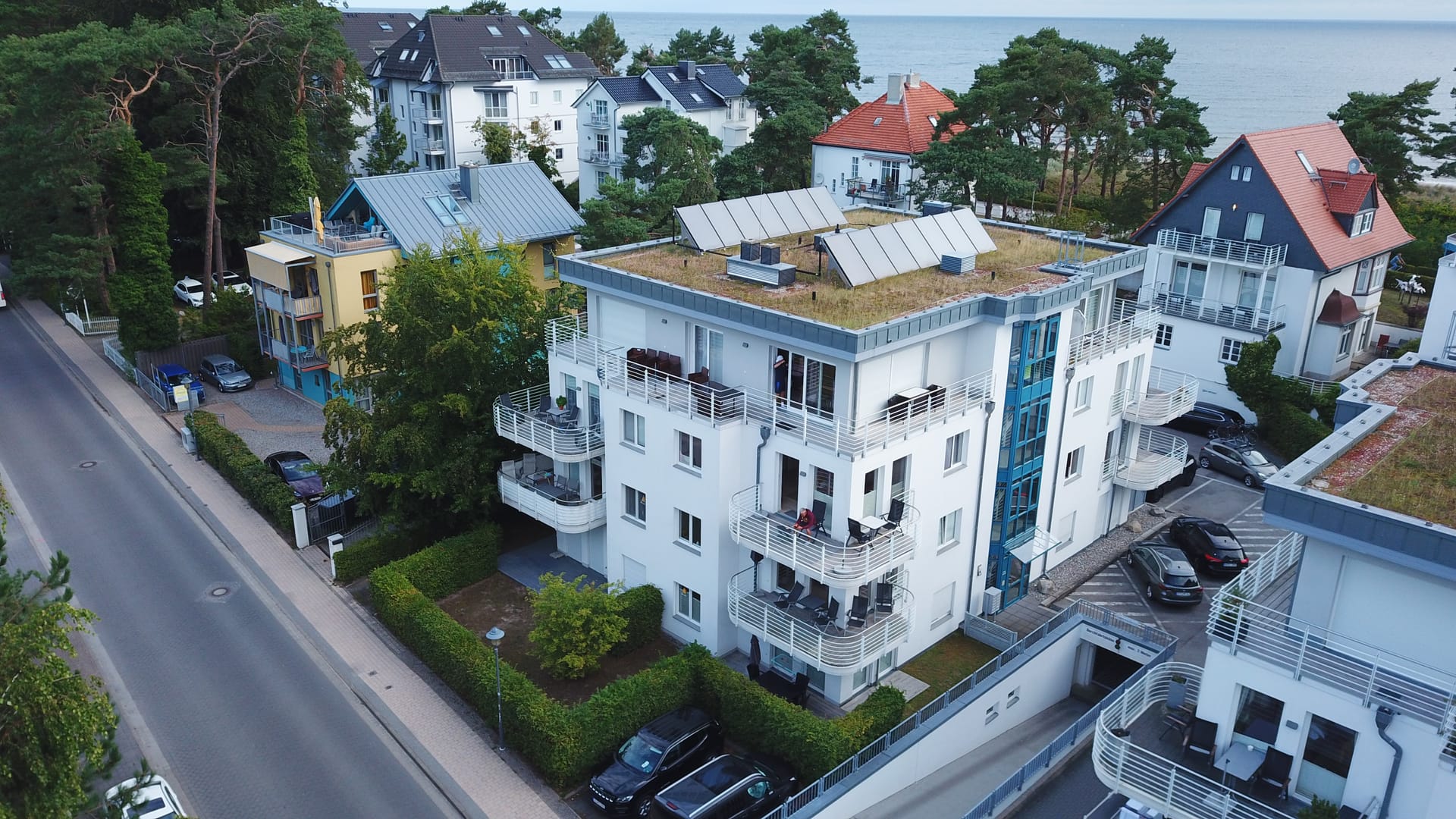 Seeresidenzen Bansin von der Bergstraße aus: weißes Appartementhaus mit begrüntem Dach, dahinter die Ostsee