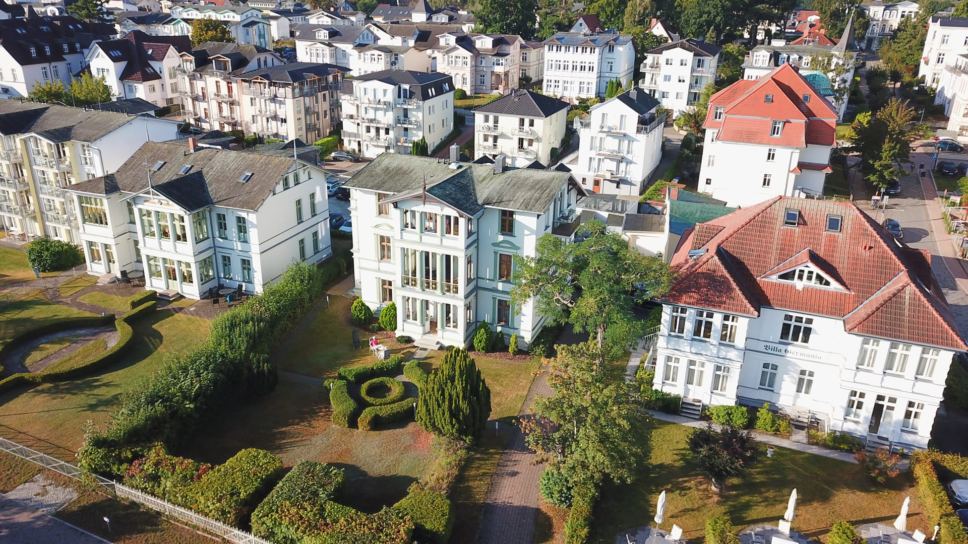 Villa Bella Ahlbeck von schräg oben: helle Fassade mit Veranden und Loggien, dahinter die Dünenstraße