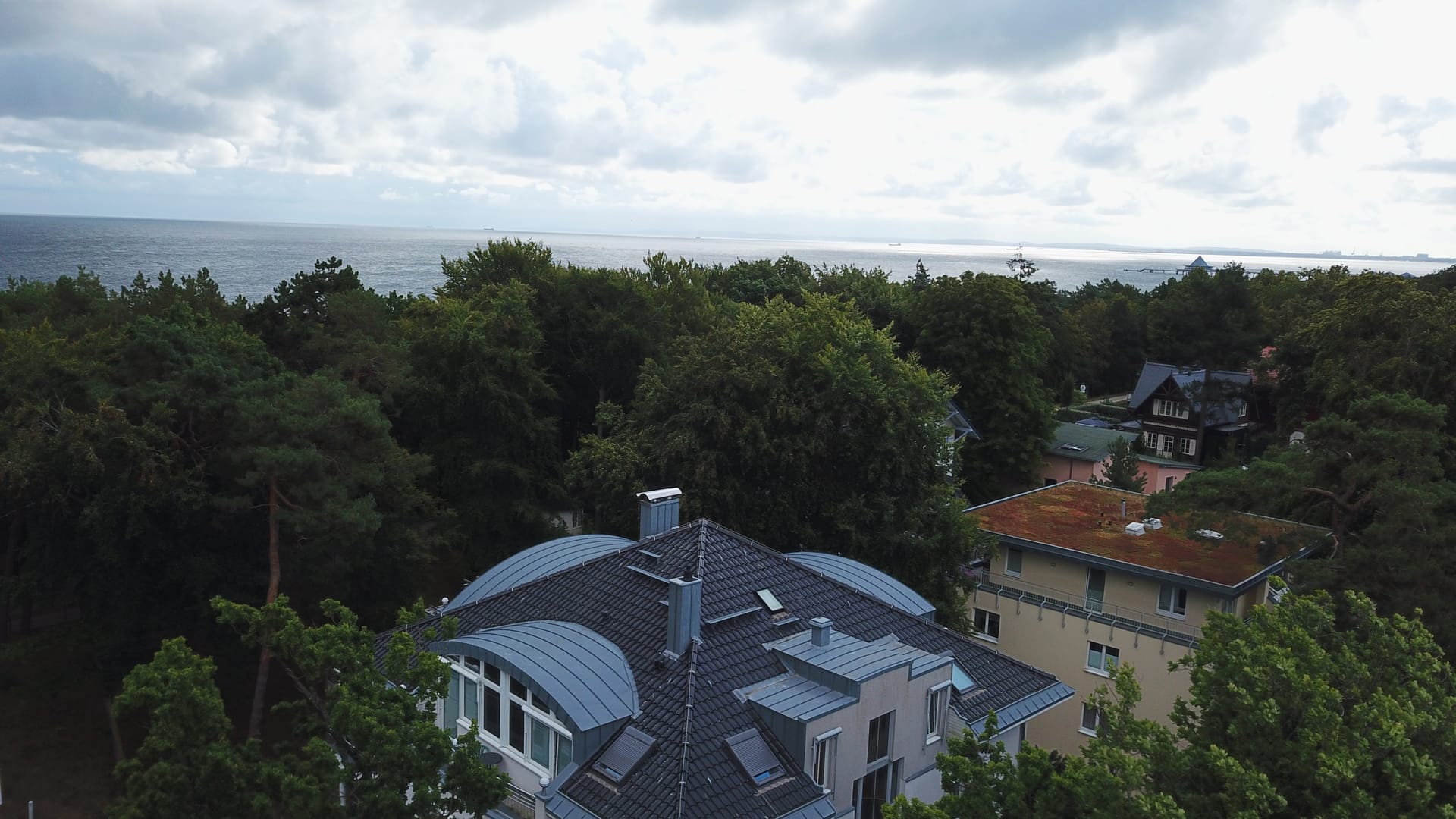 Luftaufnahme der Villa Marfa Heringsdorf – geschwungenes Dach in erster Reihe hinter der Kieferndüne, dahinter die Ostsee