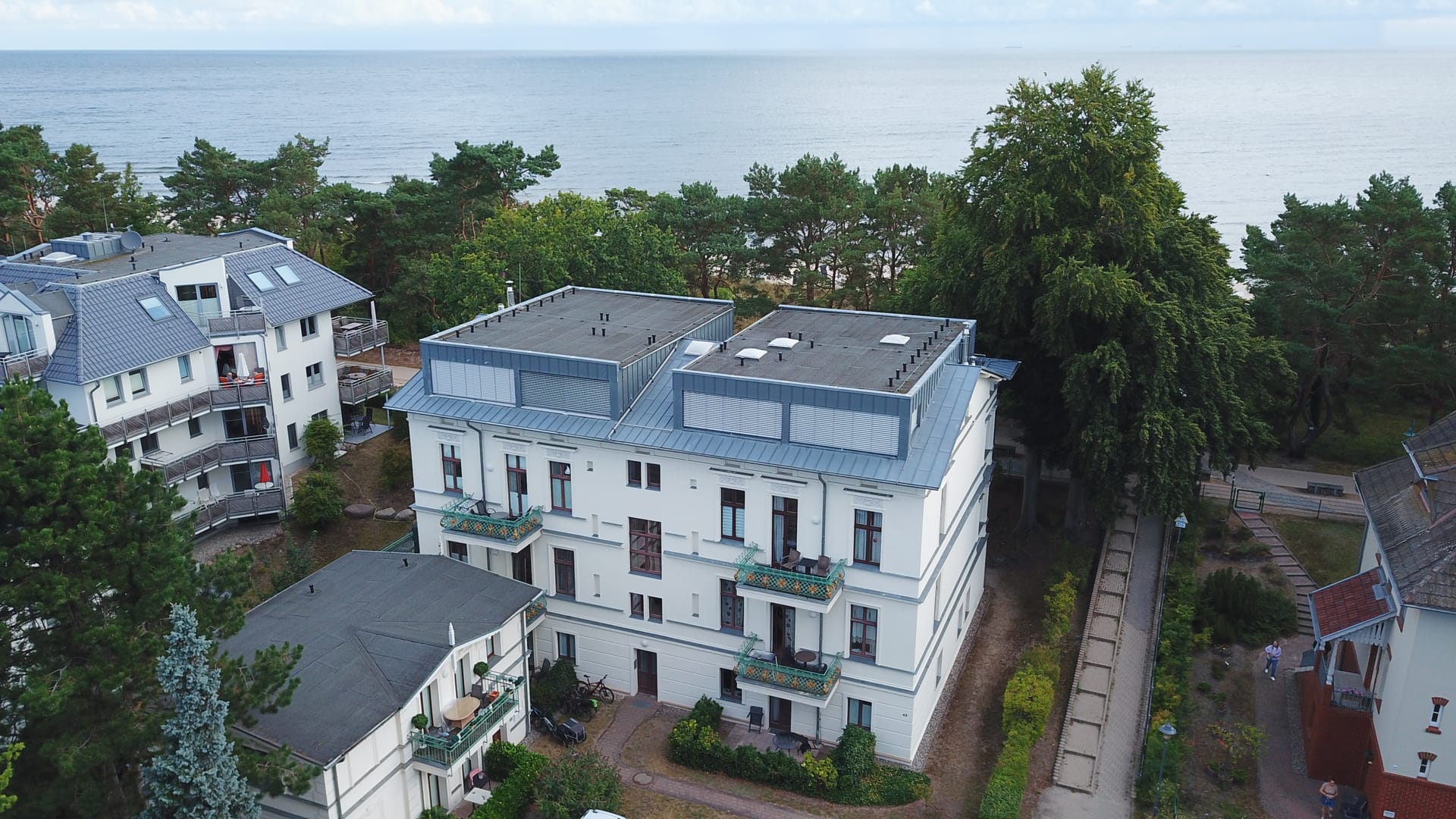 Luftaufnahme der Villa Medici Heringsdorf – weiße Bädervilla mit zwei Dachterrassen in erster Reihe, dahinter die Ostsee