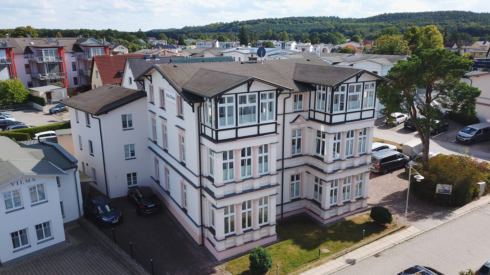 Villa Vineta Ahlbeck von oben: Straßenfassade mit Meerblick-Loggien, hinterem Anbau und Stellplätzen im Hof